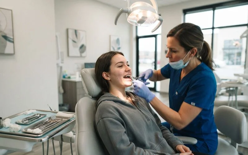 An orthodontist adjusting a wire on a patient's braces during a routine check-up visit